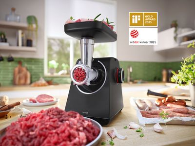 MultiPower Serie 4 z nastavkom za mletje mesa in krožnikom z mletim mesom poleg krožnika s klobasami na kuhinjskem pultu.