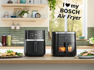 Două modele de friteuze cu aer cald Bosch aşezate alăturat pe un blat de bucătărie de culoare deschisă. L&acirc;ngă aparate sunt aşezate mai multe farfurii şi castroane cu m&acirc;ncare, inclusiv cu p&acirc;ine cu mirodenii, carne de pui, friptură şi cartofi prăjiţi, etal&acirc;nd preparatele gătite &icirc;n friteuzele cu aer cald, &icirc;n coltul dreapta sus text "I love my Bosch Air Fryer"