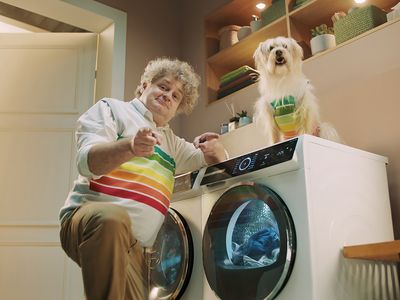 un hombre y un perro en una lavander&iacute;a moderna. A la derecha, un c&iacute;rculo verde con el texto "Reembolso hasta 150 &euro;". Detr&aacute;s, estantes con toallas y una planta.