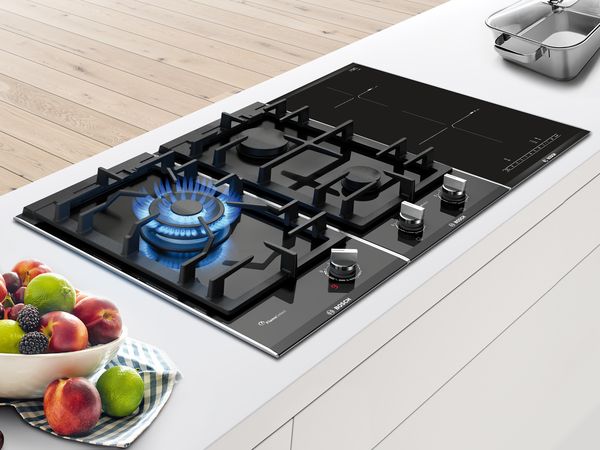 A Bosch combination gas hob with a grill, induction burner and two-flame wok burner. Steak is cooking on the grill, shrimp and vegetables on the induction.