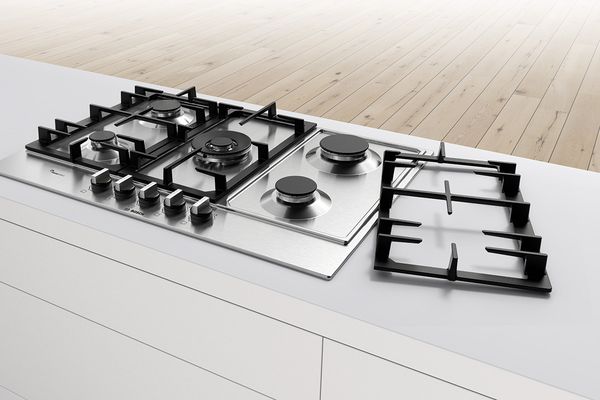 A Bosch stainless steel gas hob with the a dual pan support set to the side, demonstrating how to clean the hob.