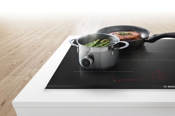 Gros plan sur une table à induction Bosch avec deux casseroles posées dessus, illustrant le choix entre une table de cuisson à gaz ou à induction.