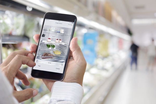 Op een smartphone wordt in de supermarkt via de Home Connect app gekeken naar de inhoud van de koelkast.