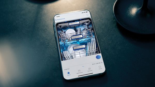 Une main tient un t&eacute;l&eacute;phone portable affichant l'application Home Connect devant un lave-vaisselle entrouvert.