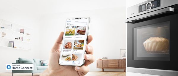 Smartphone mit Home Connect App und Backöfen von Bosch im Hintergrund. 