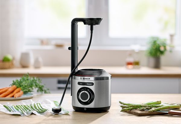 Bosch VitaMaxx auf dem Küchentisch neben frischem Gemüse und Vakuum-Reißverschlussbeutel