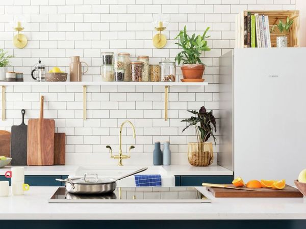 Playful and bright small galley kitchen with a white subway tile backsplash, open shelving and a cutting board with freshly sliced orange wedges on the counter