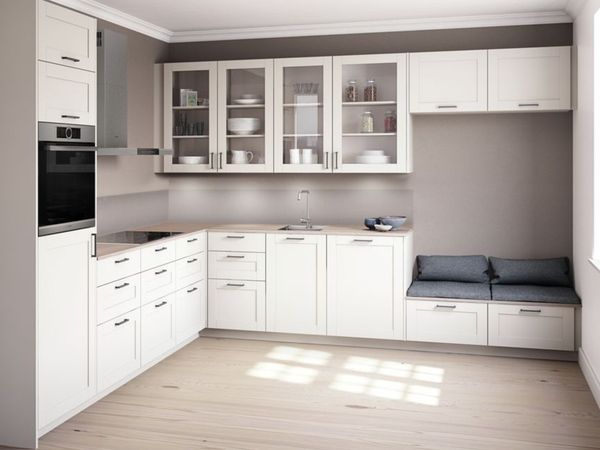 Compact farmhouse kitchen in an L-shaped layout with several overhead cabinets with glass fronts and a small reading nook