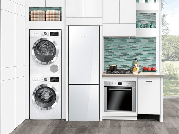 Various apartment-size home appliances in a tiny one-wall kitchen in white and a multi-color statement backsplash in various shades of green
