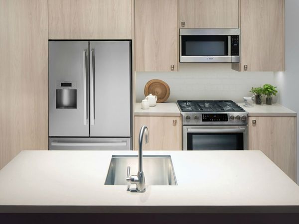 Stainless-steel fridge and small cooking appliances arranged in a perfect triangle layout with a sink placed on an island at center front.
