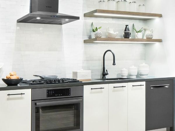 Small, modern black and white one wall kitchen with built-in cooking appliances and white crockery on open shelves.