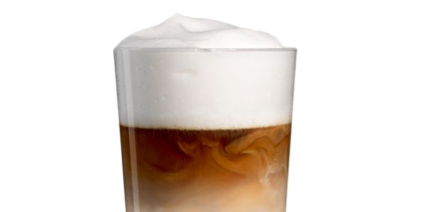 Morbida schiuma di un cappuccino versato in un bicchiere alto  