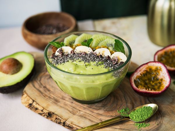 green smoothie bowl on wooden plate with avocado, kiwi, chai seeds, banana and passion fruit