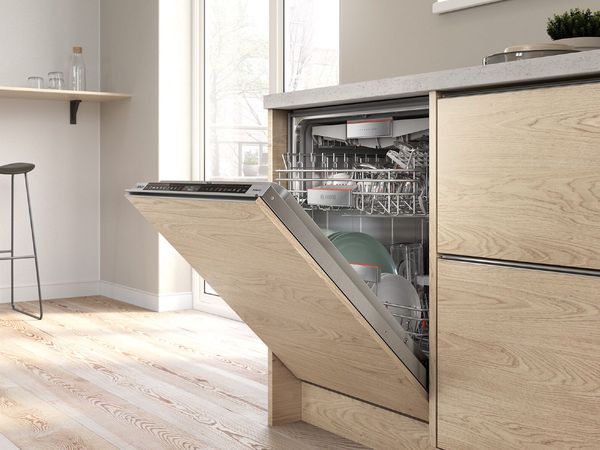 Built-in dishwasher in a modern, light-flooded kitchen with oak cabinetry and a small bar-height seating area 
