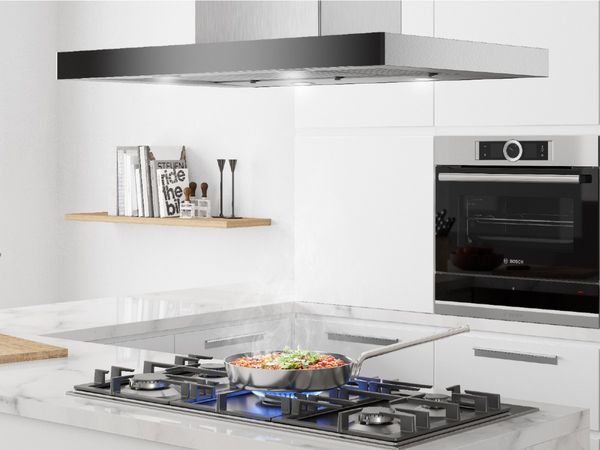 Steamy pasta dish on a 5-burner gas island hob in a cosy U-shaped kitchen with marble counters and built-in home appliances