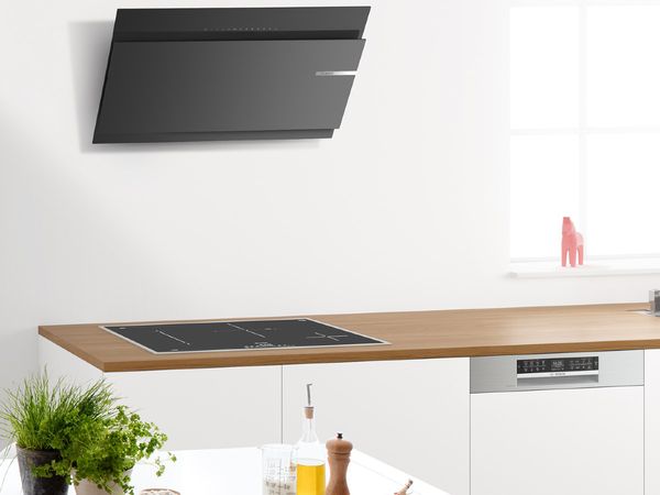 Черен, футуристичен аспиратор и елегантни домакински уреди в бяла кухня на една стена до кухненска маса със свежи билки и подправки