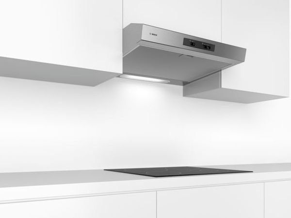 Cocina blanca de una sola pared con placa de inducción negra en contraste y campana extractora en acero inoxidable