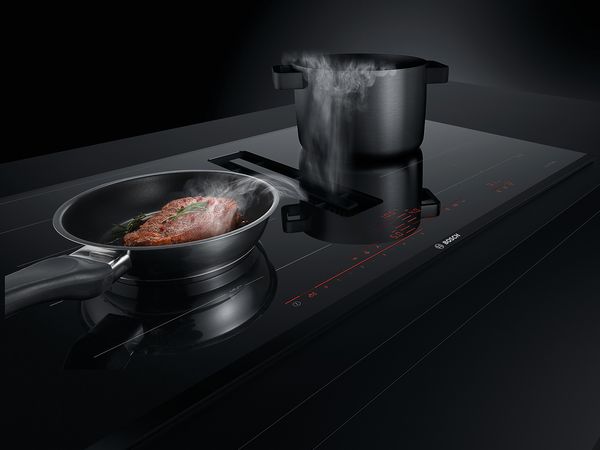 Poêle noire contenant un steak sur table de cuisson accent line de Bosch