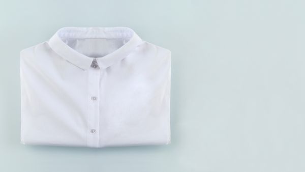 Camicia bianca piegata con colletto abbottonato su fondo chiaro