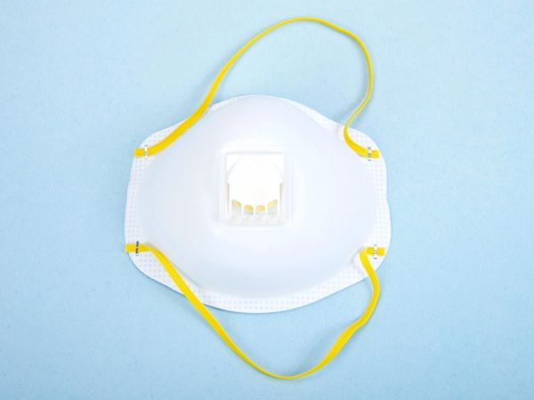 Valkoinen hengityssuojain, jossa venttiili ja keltaiset kuminauhat, sinisellä taustalla