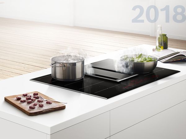 White kitchen island with an integrated ventilation cooktop absorbing steam from sauteeing vegetables.