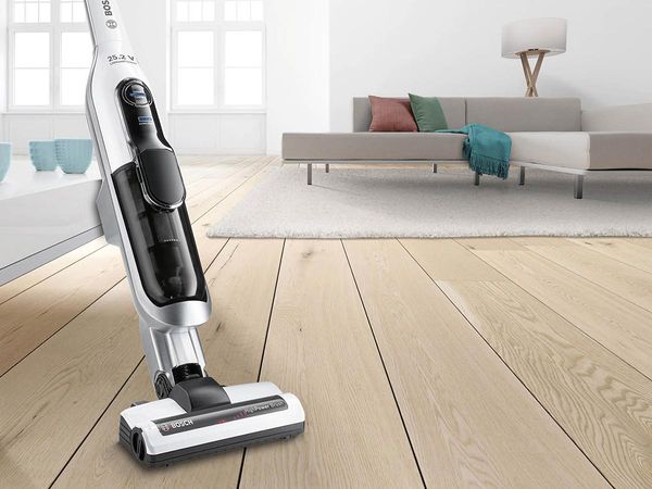 A Bosch Athlet vacuum is standing in a living room. There's a couch behind it.