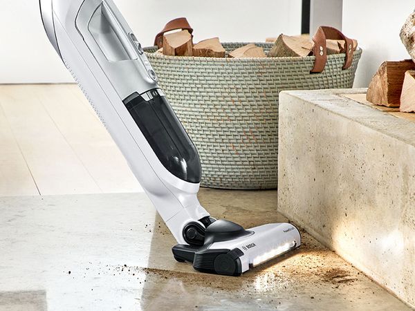 A woman vacuums confetti off the carpet with the cordless vacuum cleaner Bosch Flexxo.