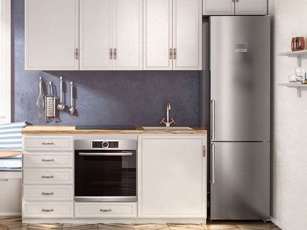 Маленька лінійна кухня в стилі заміського будинку з шафами кремового кольору, сірим фартухом і вузьким окремовстановлюваним холодильником із нержавіючої сталі впритул до стіни