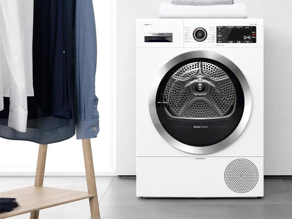 White and powerful condenser tumble dryer in a bathroom with marble tiles and oak shelves