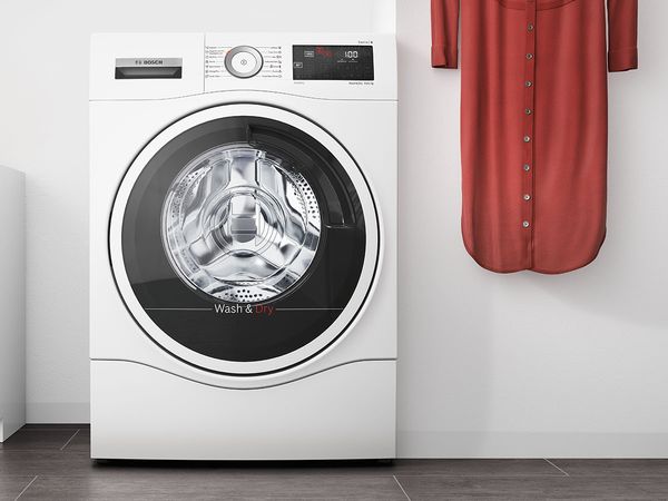 White washer dryer next to a red tunic hanging on the wall