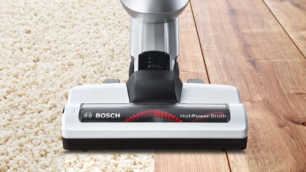A vacuum cleaner brush moves over carpet and wooden floor.
