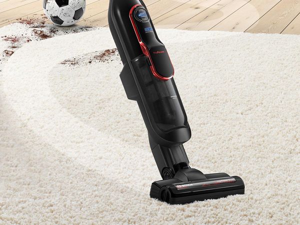 A cordless vacuum cleaner with extra suction  vacuums a carpet, making it cleaner.
