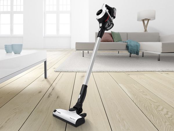 A cordless vacuum cleaner stands in the middle of a living room.