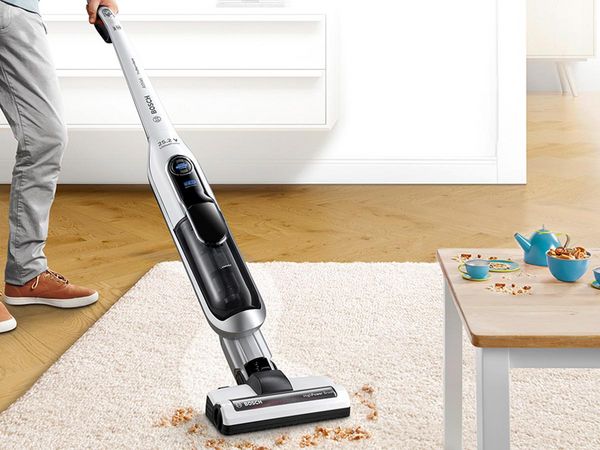 A man vacuums crumbs from a carpet. Next to it is a table with toys.