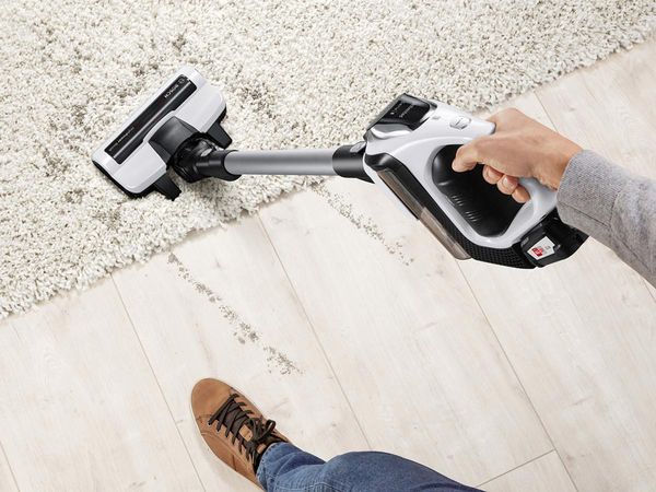 A Bosch cordless vacuum cleans dirt from the wooden floor and carpet.
