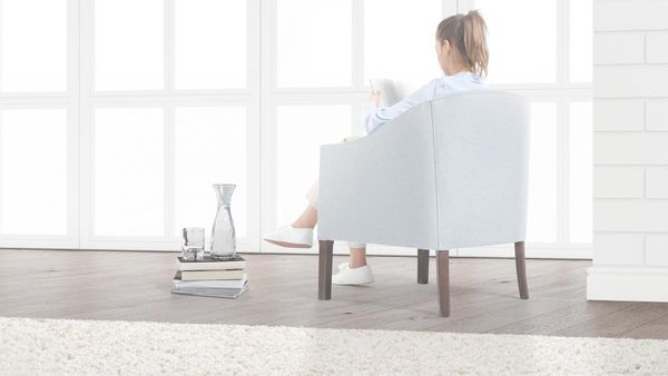 Eine Frau sitzt in einem Sessel.  Neben ihr auf dem Fußboden befinden sich Bücher und ein Glas Wasser.