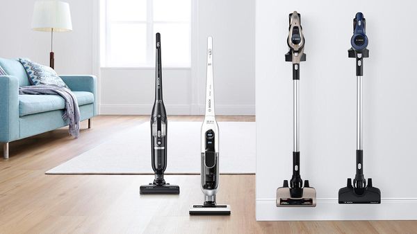 Four different cordless vacuum cleaners stand side by side in a bright room.