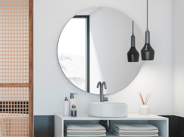 Sort loftslampe foran et stort spejl i et lille badeværelse med moderne, dekorative elementer.