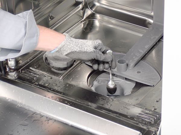 Eine Hand im Schutzhandschuhe hebelt die Pumpenabdeckung eines Bosch Geschirrspülers ab.