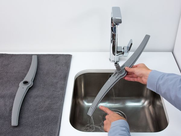 Person cleaning a dishwasher spray arm under running water. 