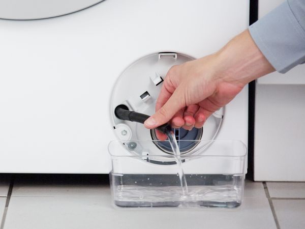 En person holder en tømmeslange til en Bosch vaskemaskin med vann som tømmes ned i en bolle