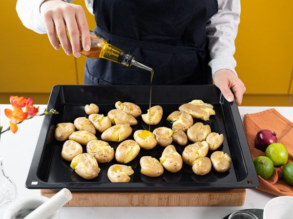 Drizzling olive oil over smashed potatoes on a ovenproof tray