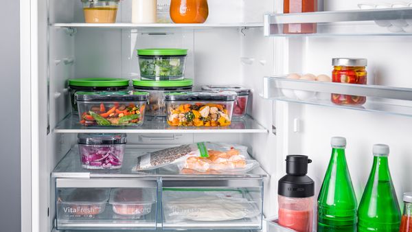Отворен хладилник с кутии за вакуумно съхранение, пълни с храна