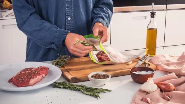 The marinated meat is being put into a vacuum bag along with some fresh herbs.