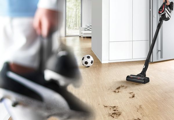 Moški uporablja brezžični sesalnik Unlimited ProPower Bosch za čiščenje umazanije z nogometnih čevljev in žoge