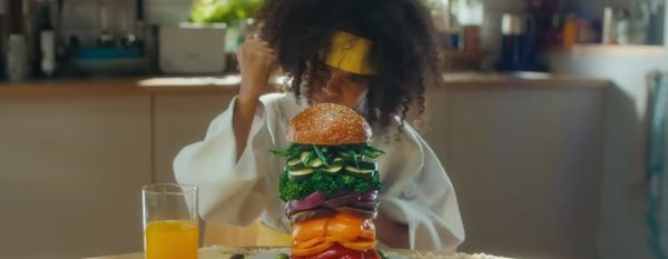 Дете в екип за джудо се радва на огромен хамбургер, пълен само със зеленчуци.