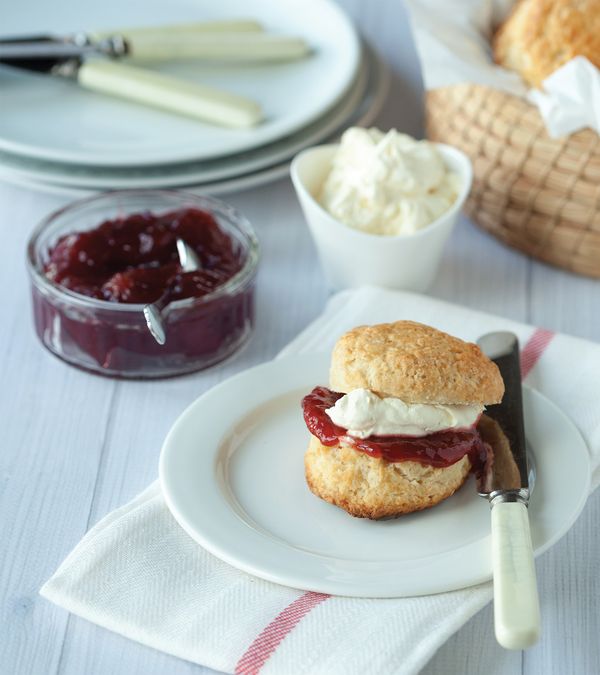 Filled scone on a plate with cream and jam in nearby dishes