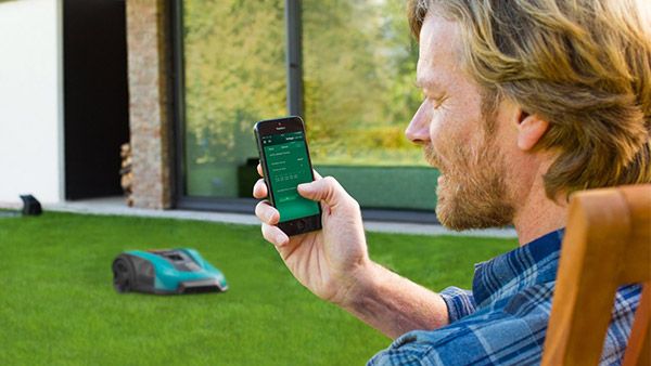 Mand, der styrer robotgræsslåmaskine fra Bosch med app på smartphone