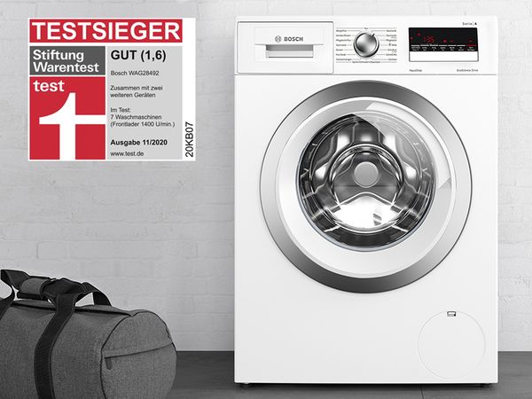 Bosch brīvstāvošā veļas mazgājamā mašīna, kuras kreisajā pusē atrodas sporta soma, un labāko testa sasniegumu nozīmīte 