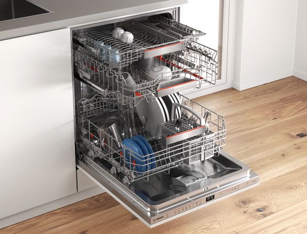 A woman kneels in front of her PerfectDry Bosch dishwasher, looks into the camera and lets a blue plate casually circling on her index finger of the right hand. The left hand index finger points at the plate and shows how easy it is to clean the dishes and save energy. 